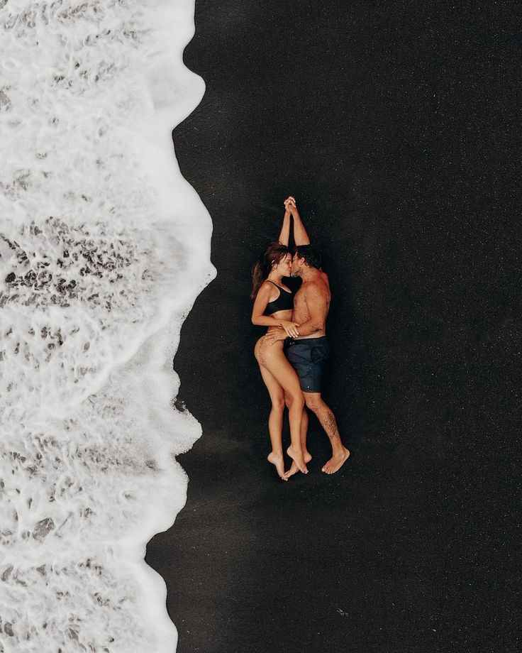 two people standing on the beach with their arms around each other