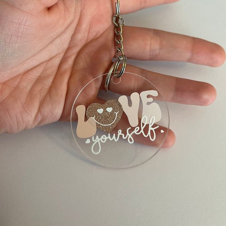 a hand holding a keychain with the words love yourself on it and a smiling face