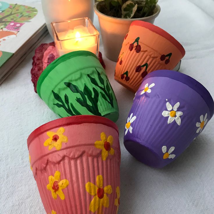 four flower pots are sitting on a table next to a lit candle and some books