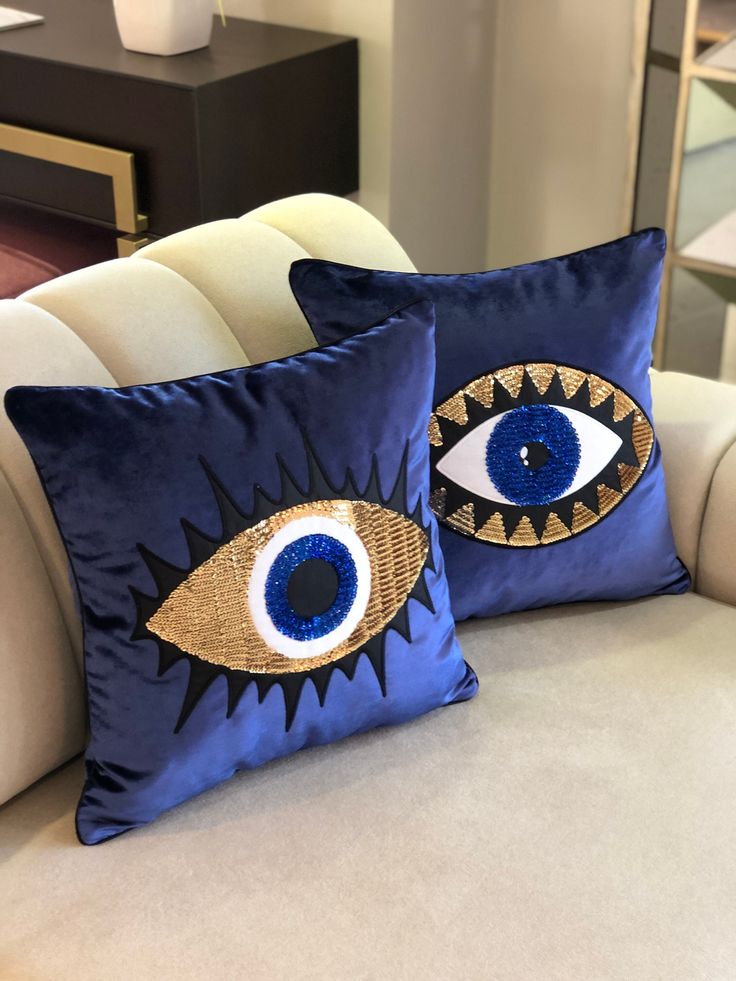 two blue pillows with an evil eye on them sitting on a white couch in a living room