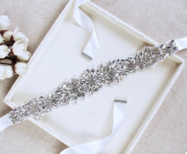 Add a touch of classic elegance to your bridal gown with this sparkling beaded belt! Adorned with an array of glowing crystals on a silver base, it will give your dress an extra touch of glam to finish off your perfect look on your wedding day. The crystal appliqué measures 10.6" (approx. 27cm) long by 1.5" (approx. 4cm) wide. It can be ordered as appliqué only to be sewn onto your dress, or attached to your choice of white or ivory double-faced satin ribbon, 1.5" wide and with a total length of Elegant Silver Bedazzled Sash, Elegant Silver Bedazzled Bridal Accessories, Elegant Silver Bedazzled Sashes, Elegant Bedazzled Silver Bridal Accessories, Elegant Bedazzled Silver Sash, Elegant Bedazzled Silver Sashes, Elegant Silver Belt With Rhinestones, Silver Bedazzled Bridal Belt For Wedding, Silver Fitted Bridal Belt For Formal Occasions