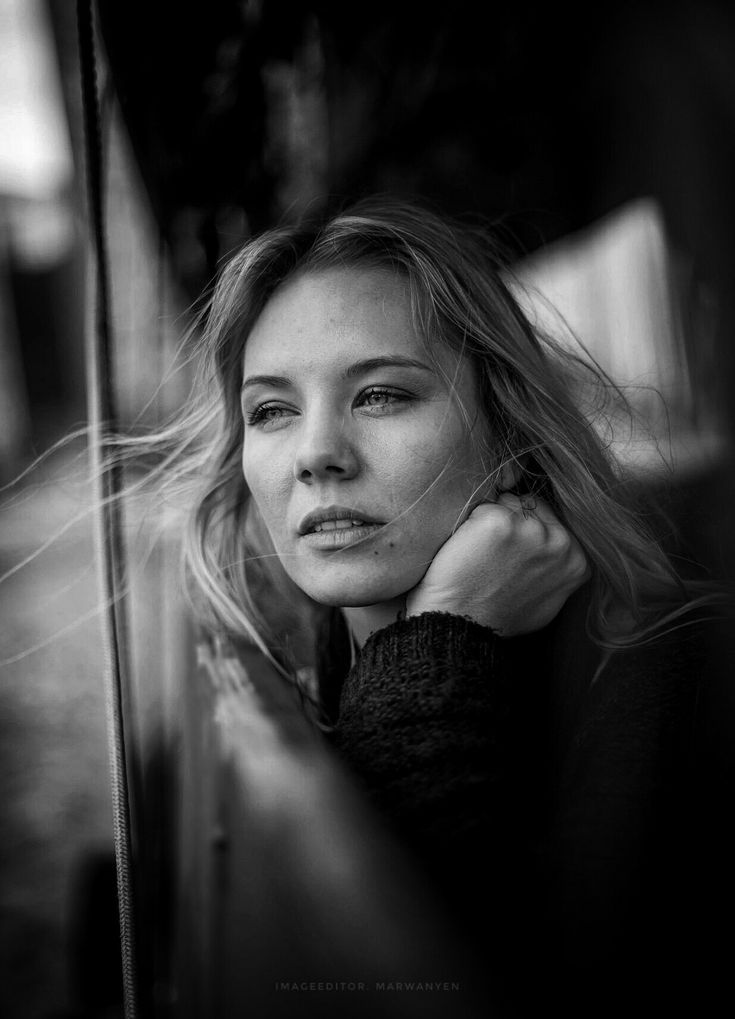 a black and white photo of a woman leaning against a wall with her hair blowing in the wind