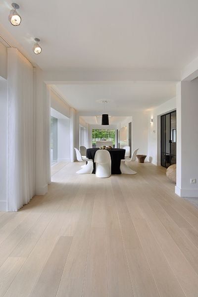 an empty living room with white walls and wood flooring on the side, along with large windows