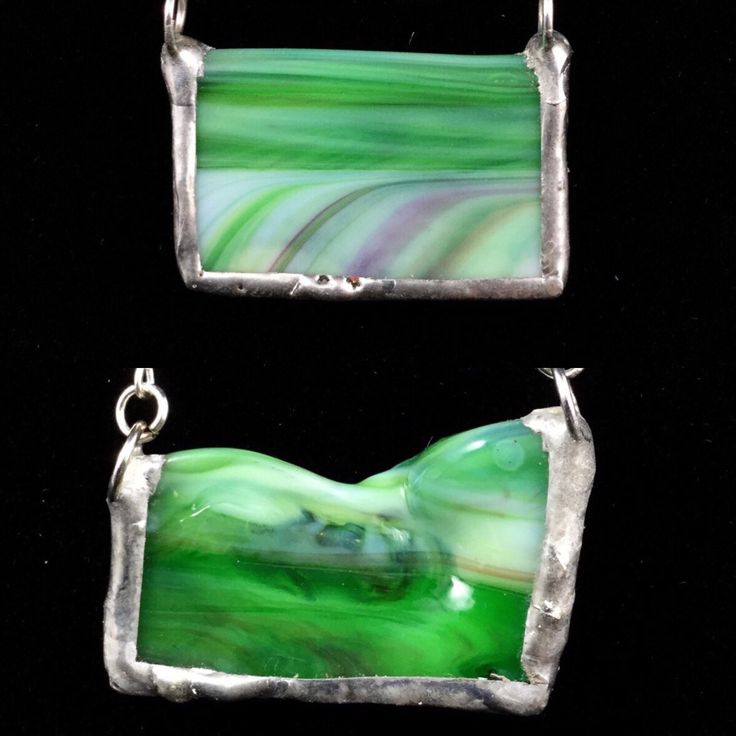 "For my necklaces, I work with handmade art glass, looking for the pieces with the most interesting patterning to create truly unique, one-of-a-kind pendants. This piece of glass is a piece of raw edge, where molten glass cooled, forming a smooth, ruffled border that I have left open on the top of the piece. This glass' green colour is streaked with white and hints of red. It is cut directly into the chain. I have cut two of these from different parts, giving each a different contour and shading. The straight pendant is rectangular, with a straight, smooth top edge and very defined streaks. It measures 1-1/4\" wide by 13/16\" high. The curvy pendant has a border featuring swoops and a bend in the glass, giving it a highly quirky feel. It .measures 1-1/4\" wide by 3/4\" high. Each hangs on Artisan Green Recycled Glass Jewelry, Unique Glass Pendant Necklace, Unique Glass Pendant Necklaces, Handmade Glass Jewelry For Collectors, Glass Pendant Necklace With Cabochon, Green Glass Pendant Jewelry, Unique Glass Pendant Jewelry, Artsy Glass Jewelry For Jewelry Making, Unique Green Square Pendant Jewelry