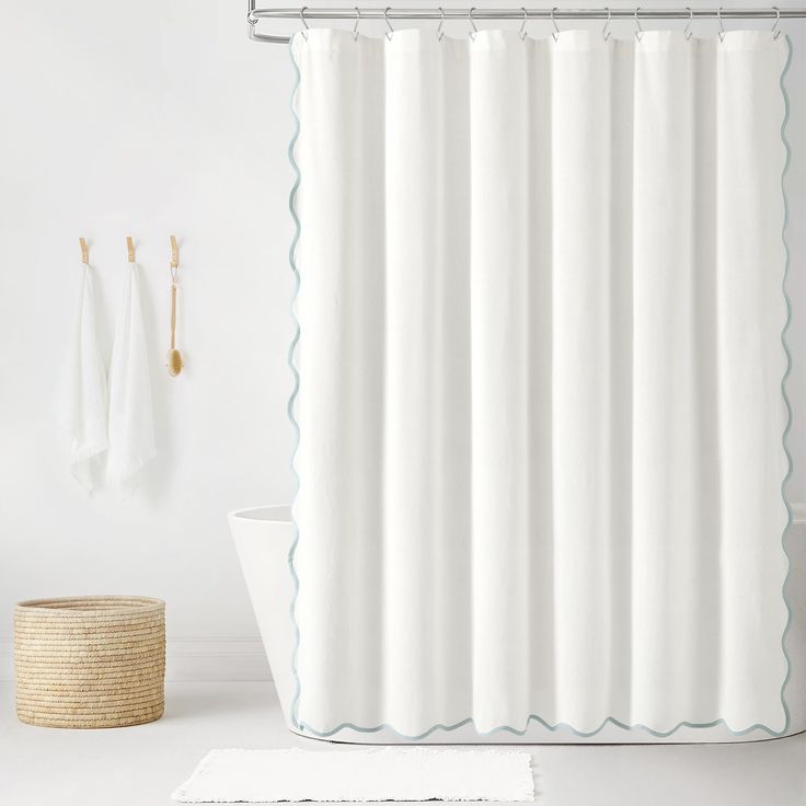 a white shower curtain with blue scalloped trim in a bathroom next to a basket