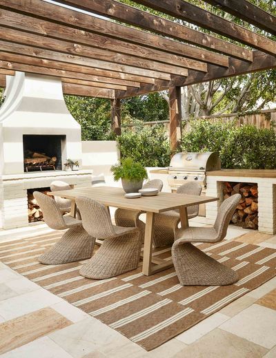 an outdoor dining table with chairs and a potted plant on the end, in front of a fireplace