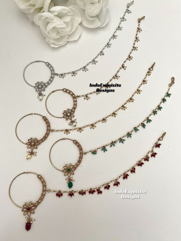 four different types of hoop earrings and necklaces with flowers on the table in the background