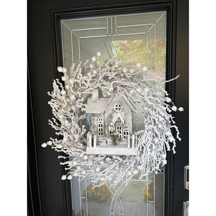 a wreath made out of fake branches on a front door with a house in the background