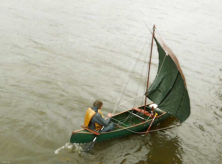 two people in a small green sailboat on the water with one person wearing a life jacket