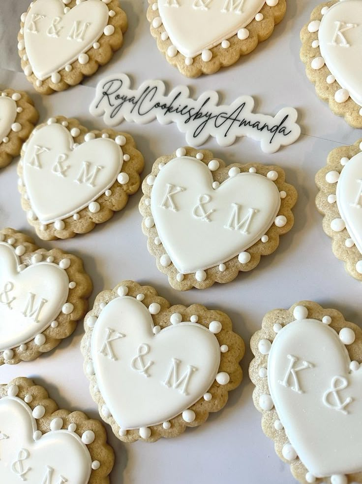 decorated cookies arranged in the shape of heart and initials on a white tablecloth with writing