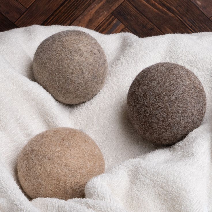 three wool balls sitting on top of a white blanket next to a wooden floor and wall