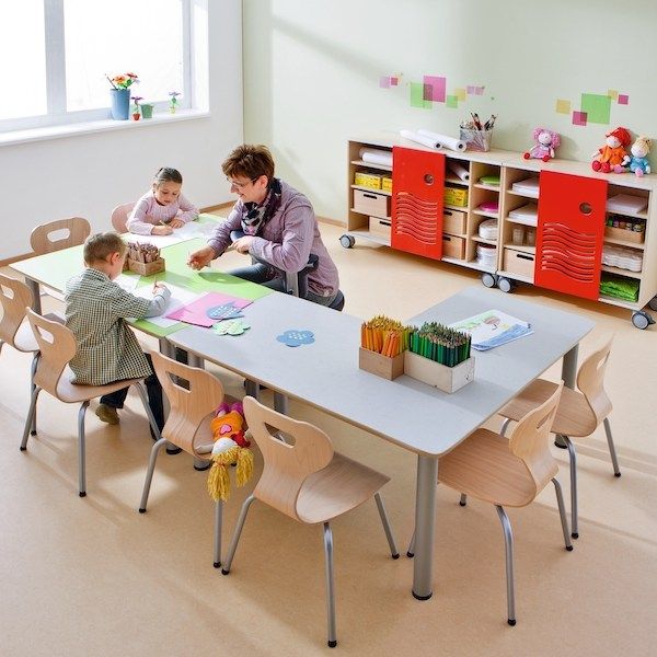 an adult and two children sitting at a table in a room with toys on the floor