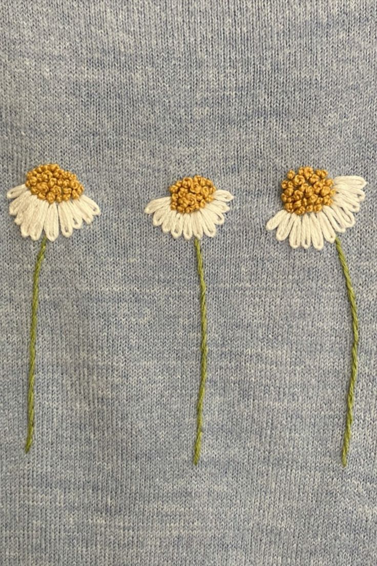 three white daisies on a blue sweater with green stems sticking out of the middle