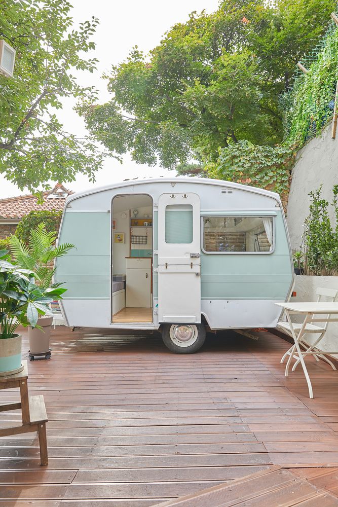 an old camper trailer is parked on the deck in front of some trees and chairs