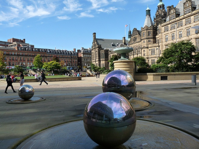 three shiny balls sitting on top of a fountain in the middle of a park with people walking around