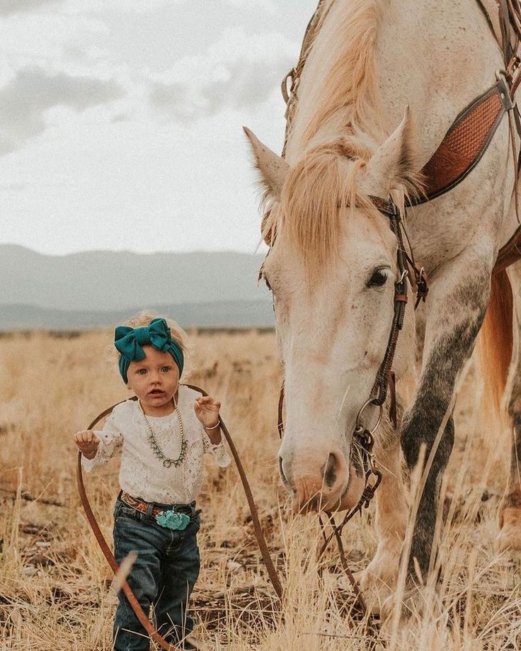 a little boy standing next to a white horse in a dry grass field with mountains in the background