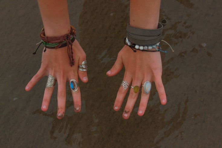 two hands with rings and bracelets on their palms are standing in the shallow water