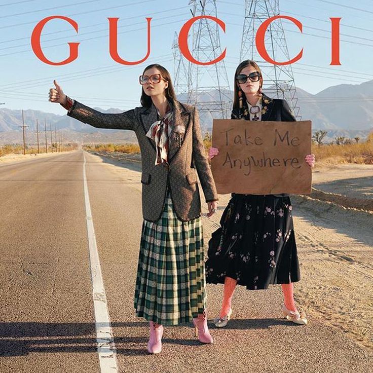 two women standing in the middle of an empty road holding a sign that says gucci