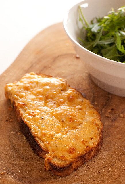 a piece of bread sitting on top of a wooden cutting board next to a bowl of greens