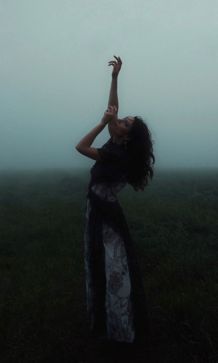 a woman standing in the grass with her arms outstretched