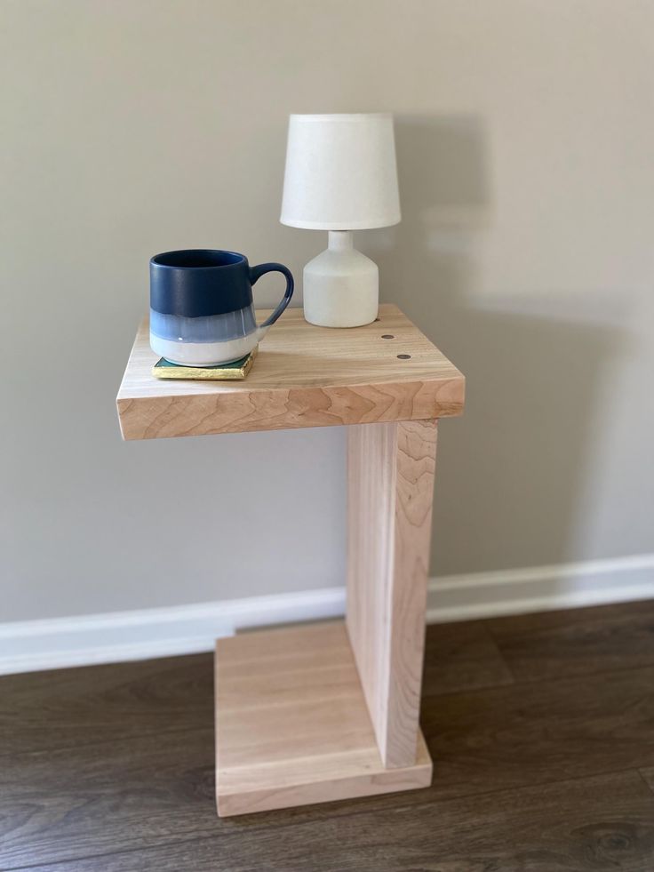 a wooden table with a blue mug on it and a white lamp next to it