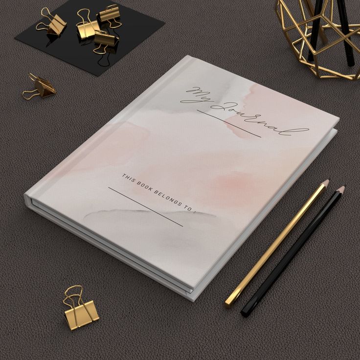 an open notebook next to some pens and other items on a table with gold accents