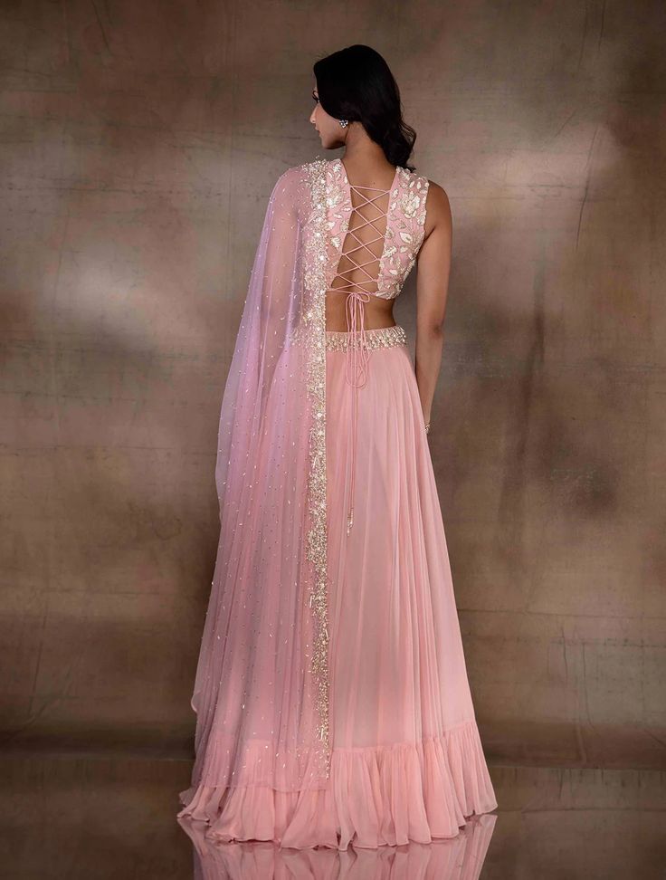 Soft pink flowy lehenga with a tiered hem featuring an ivory pearl drop embellished waistband, paired with a plunge neck tie up blouse hand embellished with ivory florals. Paired with a net dupatta hand embellished with ivory pearls, mixed materials & glass beaded tassles.From Shloka Khialani's Winter Sun collection.DELIVERY TIMEPlease allow 6-8 weeks for your outfit to arrive.FABRIC DETAILSGeorgette, Net, CrepeProfessional cleaning only. Flowy Lehenga, Tie Up Blouse, Winter Sun, Ivory Pearl, Net Dupatta, Beaded Tassels, Pearl Drop, Skirt Length, Soft Pink