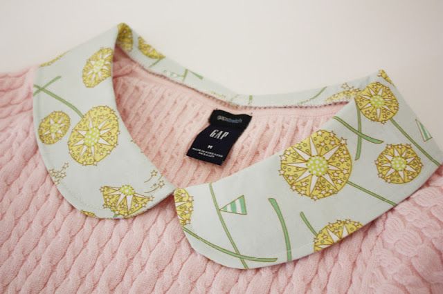 a pink sweater with yellow flowers on it and a black tag hanging from the collar