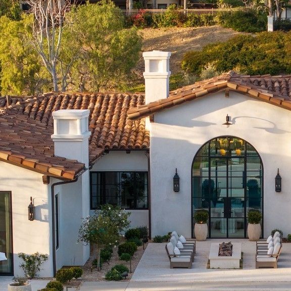 a white house with brown tile roofing and two lounge chairs in front of it