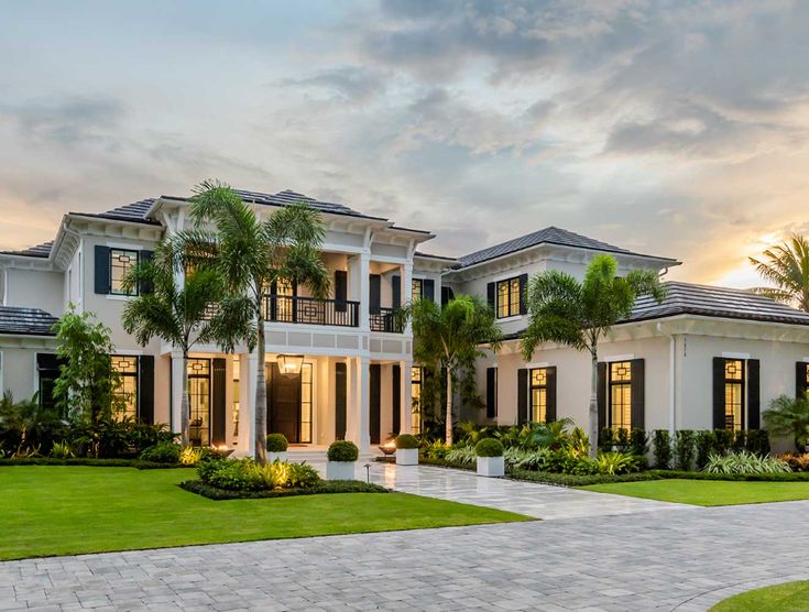 a large white house with lots of windows and palm trees in the front yard at sunset