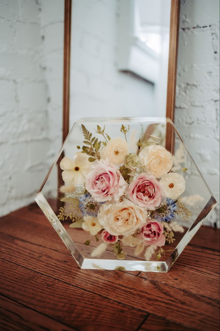 a glass vase with flowers in it sitting on a table next to a wooden mirror