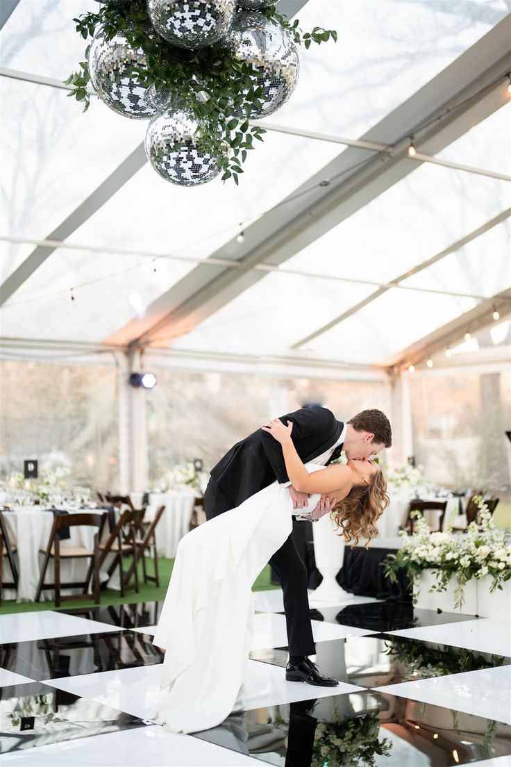 a bride and groom kissing on the dance floor at their wedding reception in a tent