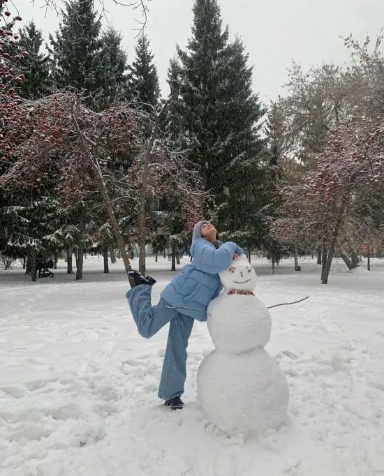 a man is making a snowman in the middle of a snowy field with trees