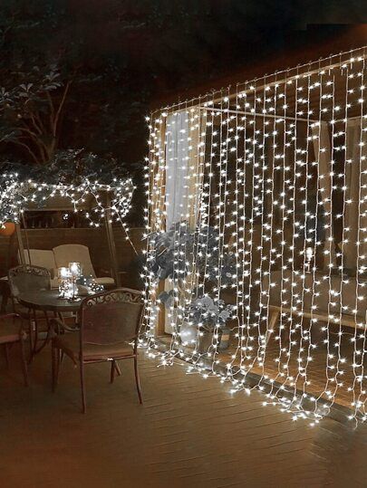 a patio covered in christmas lights and string lights on the side of it, next to a table with chairs