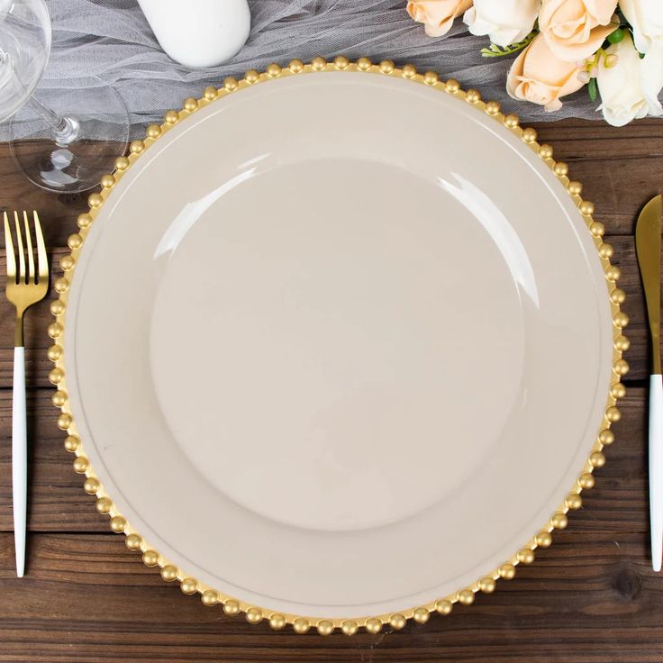 a white plate with gold trim sits on a wooden table next to silverware and flowers