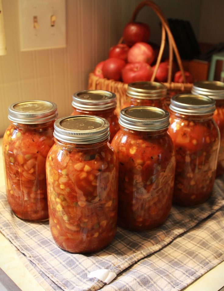 six jars filled with food sitting on top of a table next to apples and a basket