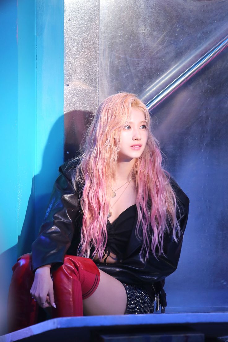 a woman with long pink hair sitting on a red chair in front of a blue wall