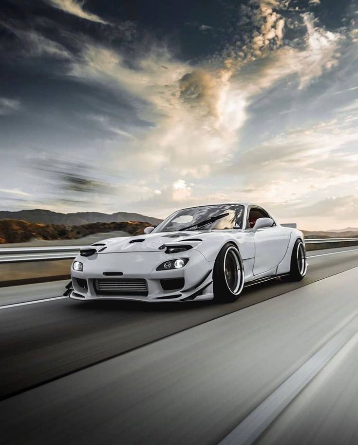 a white sports car driving down the road at high speed with clouds in the background