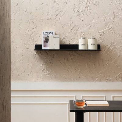 two black shelves on the wall above a table with books and cups sitting on it