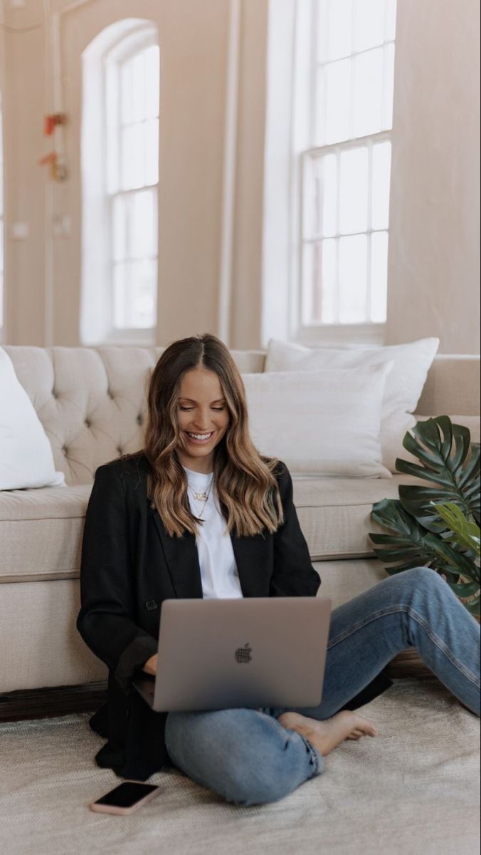 a woman is sitting on the floor with her laptop in front of her and smiling