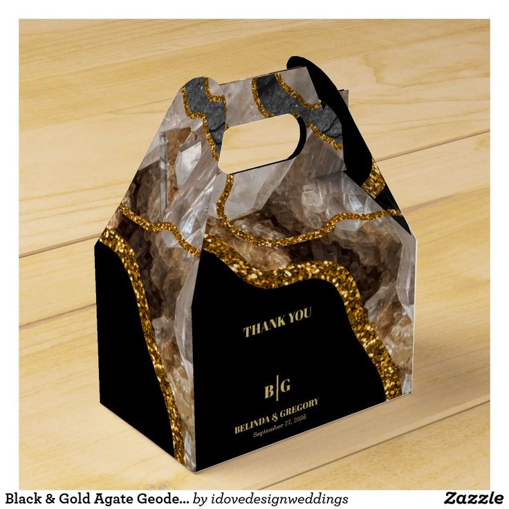 a black and gold gift bag with golden sequins on the handle sitting on a wooden surface