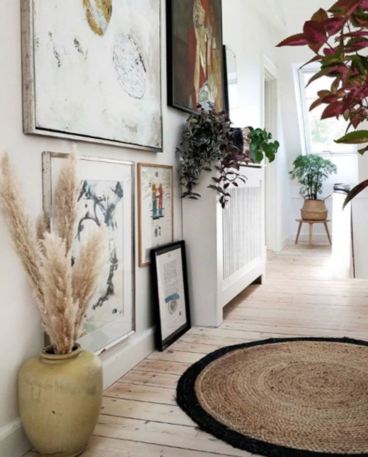 a hallway with pictures on the wall and plants in a vase next to it,