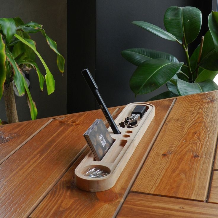 a wooden desk with a cell phone, pen and pencil holder sitting on top of it