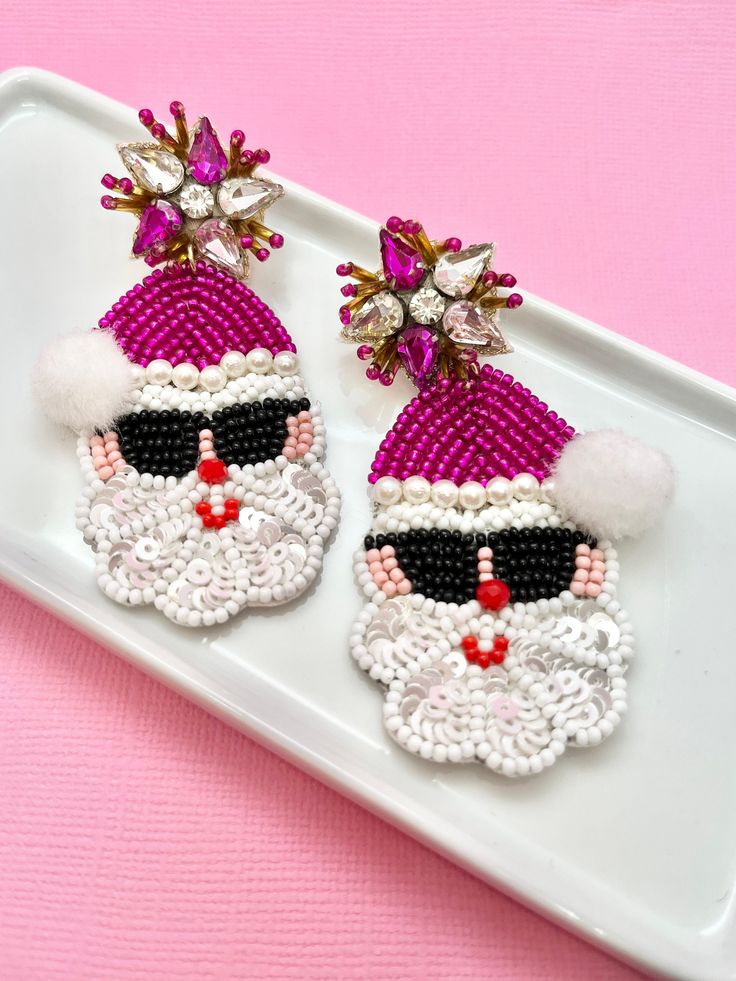 pair of santa claus earrings on white tray with pink background and gold trimmings