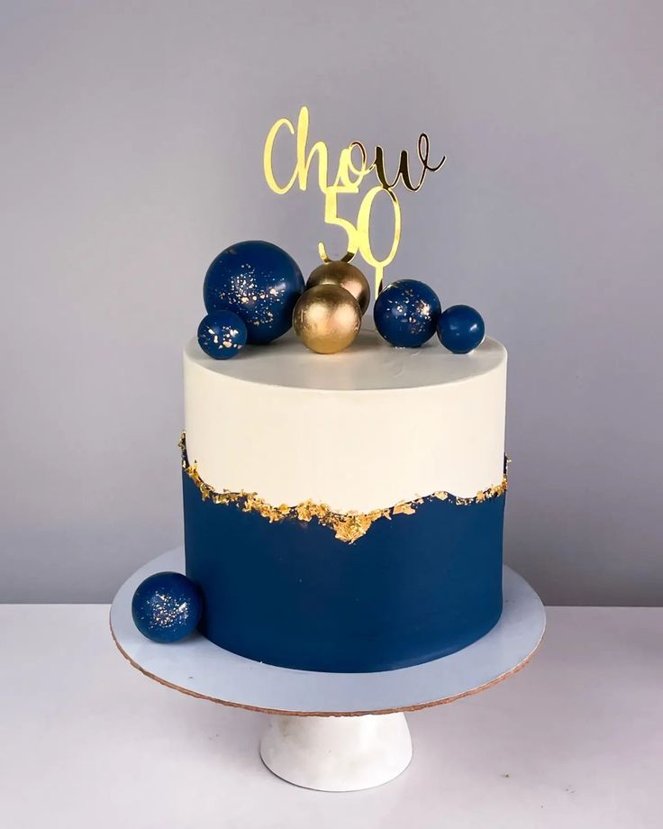 a blue and white cake with gold decorations on top that says chee 50 in the middle