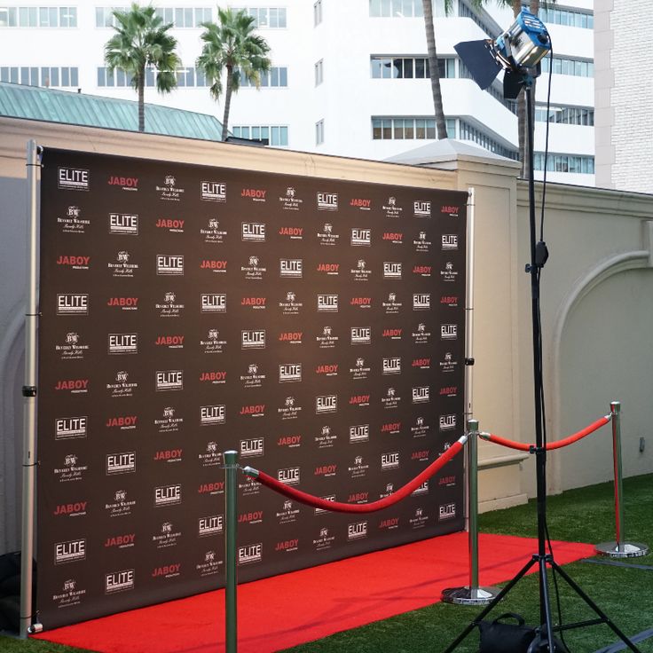 a red carpeted area in front of a brown backdrop with white lettering and palm trees