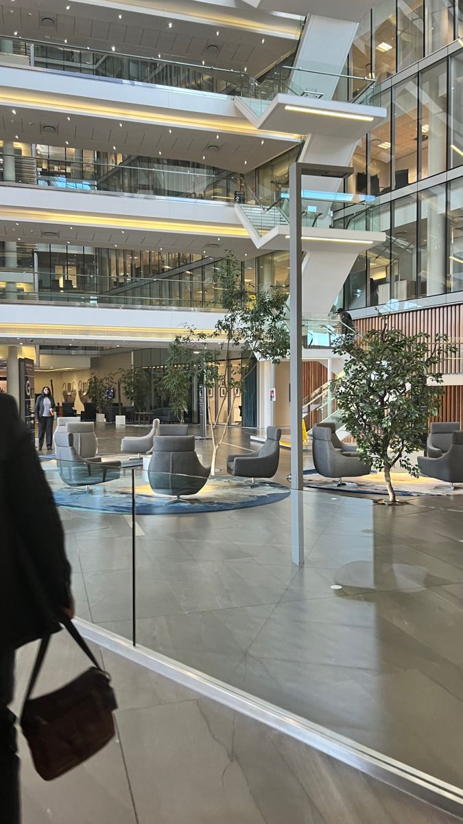 a woman is walking through the lobby of an office building with glass walls and balconies