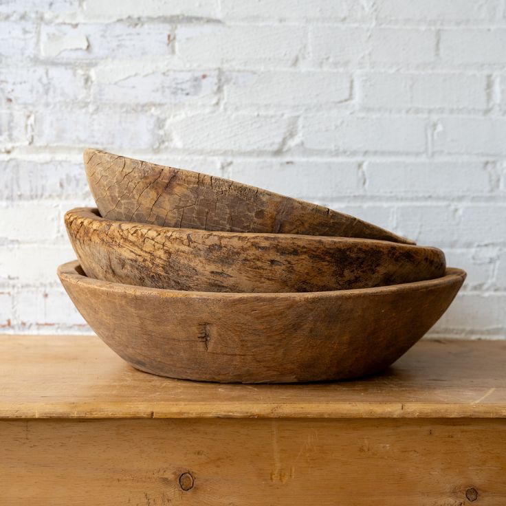 three wooden bowls sitting on top of a wooden table next to a white brick wall