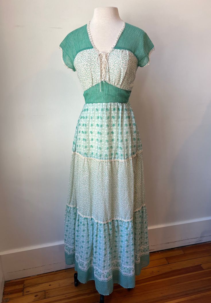 This is such a lovely 70s floral maxi dress! This tiered dress has a unique lace up bodice that is adjustable. This floral dress is made of a soft cotton. The pattern is of beautiful green and white flowers and stripes! It has cap sleeves with white lace trim and a sash that ties in the back. This dress has a zipper with a hook to secure in the back and is fully lined as well. The perfect dress to throw on in the Summer or Spring. This dress is just so pretty! Imagine all the complements and conversations you will have wearing this dress! You will know you are the only one on earth who owns this special piece. To have a one of a kind... that is the magic of Vintage!  Tags: N/A Material: Cotton Size: 4/6 Measurements:  Bust: 34.5" Waist: 28" Hips:  45" Length: 59" CONDITION: Very good! Bare Bohemian Maxi-length Prairie Dress For Garden Party, Bohemian Prairie Maxi Dress For Garden Party, Bohemian Maxi Prairie Dress For Garden Party, Bohemian Maxi Dress With Empire Waist For Garden Party, Fitted Bohemian Prairie Dress, Midi Length, Green Maxi Dress With Lace Trim For Spring, Spring Bohemian Empire Waist Maxi Dress, Vintage Beach Maxi Dress With Lace Trim, Vintage Lace Trim Maxi Dress For Beach