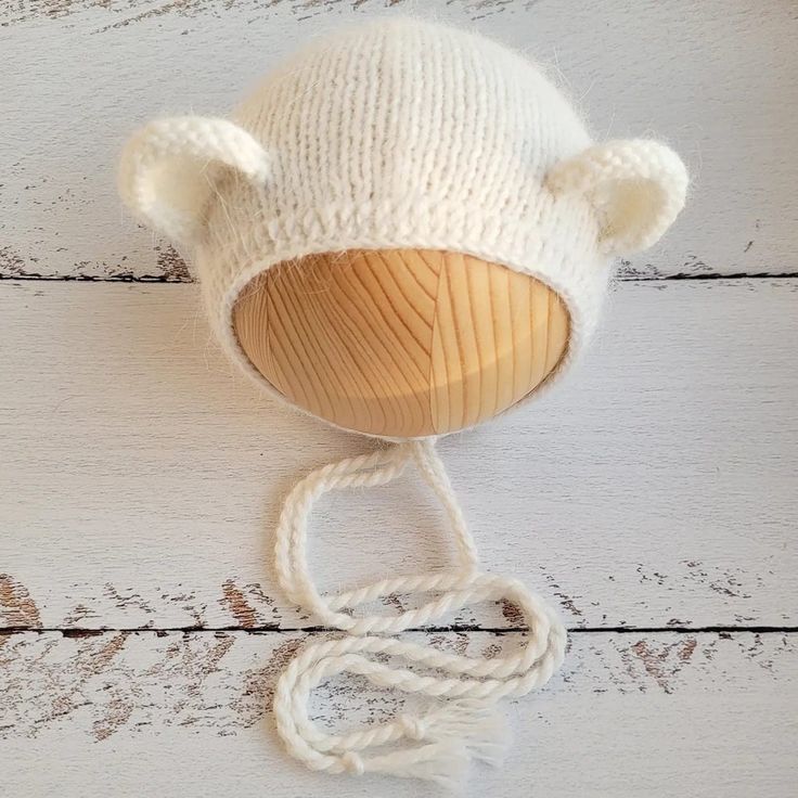 a white knitted bear hat on top of a wooden string with a knot around it